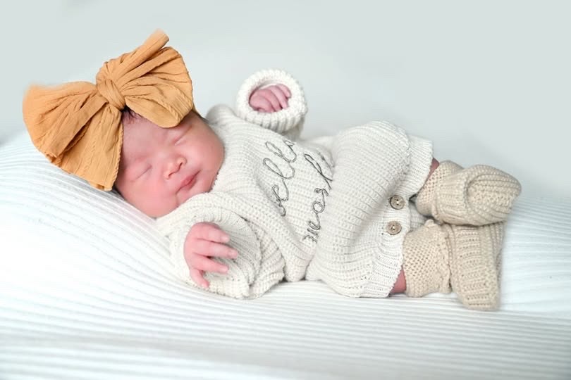 Newborn Laila asleep with a big mustard bow
